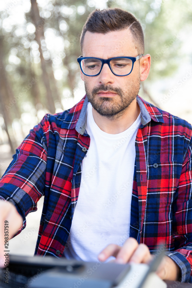 Joven con gafas concentrado escribiendo un libro a maquina de escribir al aire libre. Joven con gafas concentrado escribiendo un libro a maquina de escribir al aire libre.