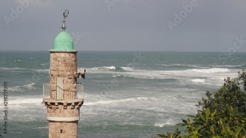 Close up of a Mosque tower, watching over the mediterranean sea, in the old city of Jaffa. Strong waves, of after a storm, in the background.