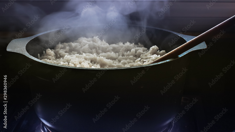 Cocinando arroz en una olla negra con cuchara de madera Cocinando arroz en una olla negra con cuchara de madera