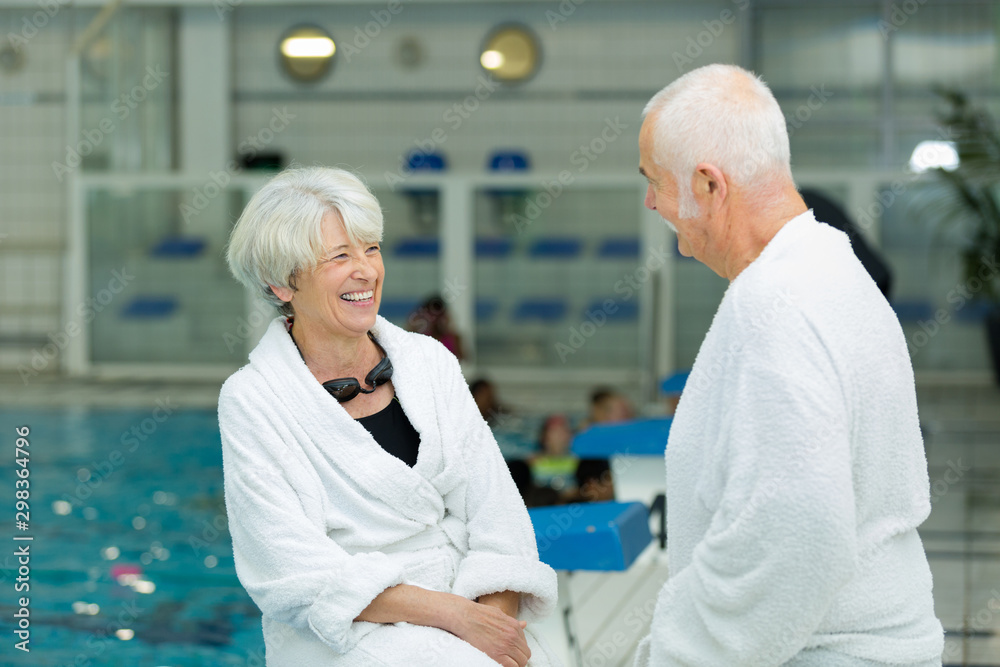 Obraz premium senior couple wearing bathrobes laughing by side of indoor pool
