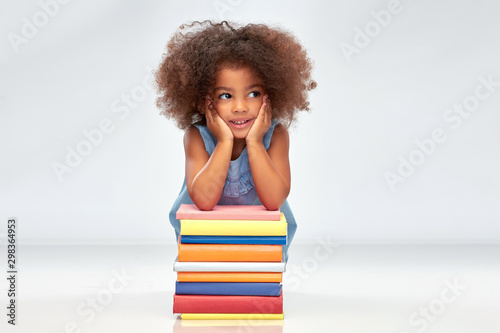 childhood, school and education concept - happy smiling little african american girl with pile of books over grey background