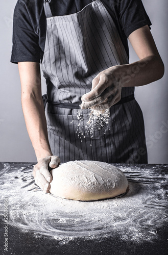 Posypywanie mąką chleba lub ciasta przez kucharza na ciemnym stole