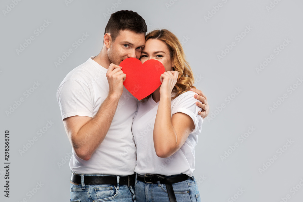 love, valentines day and relationships concept - smiling couple hiding behind big red heart over grey background love, valentines day and relationships concept - smiling couple hiding behind big red heart over grey background