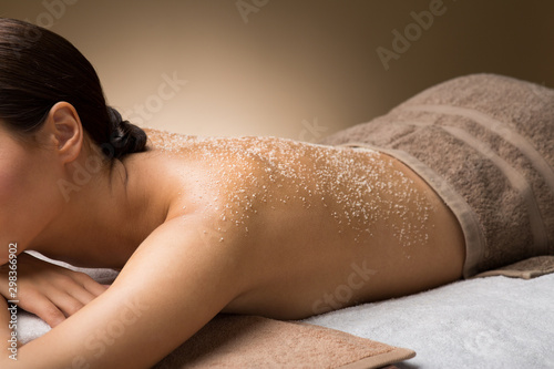 wellness, beauty and relaxation concept - close up of beautiful young woman with sea salt on skin at spa