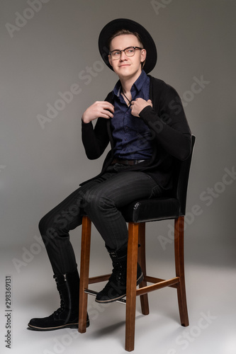 Brunet man in a casual dark clothes posing over a grey background sitting on the bar chair.