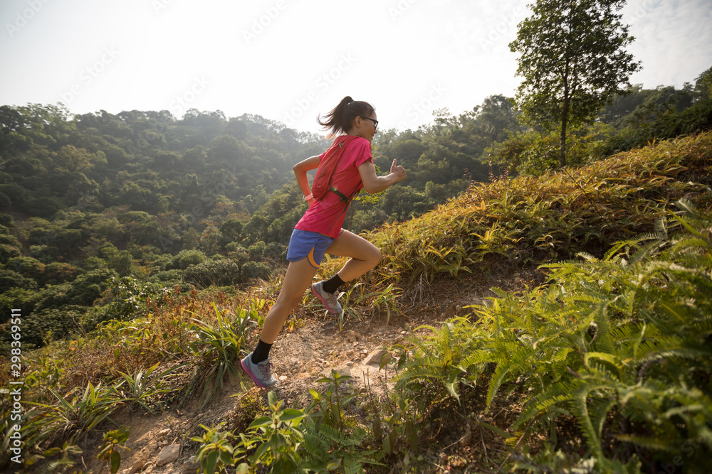 Woman ultramarathon runner running up on mountain slope in tropical rainforest