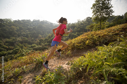 Woman ultramarathon runner running up on mountain slope in tropical rainforest