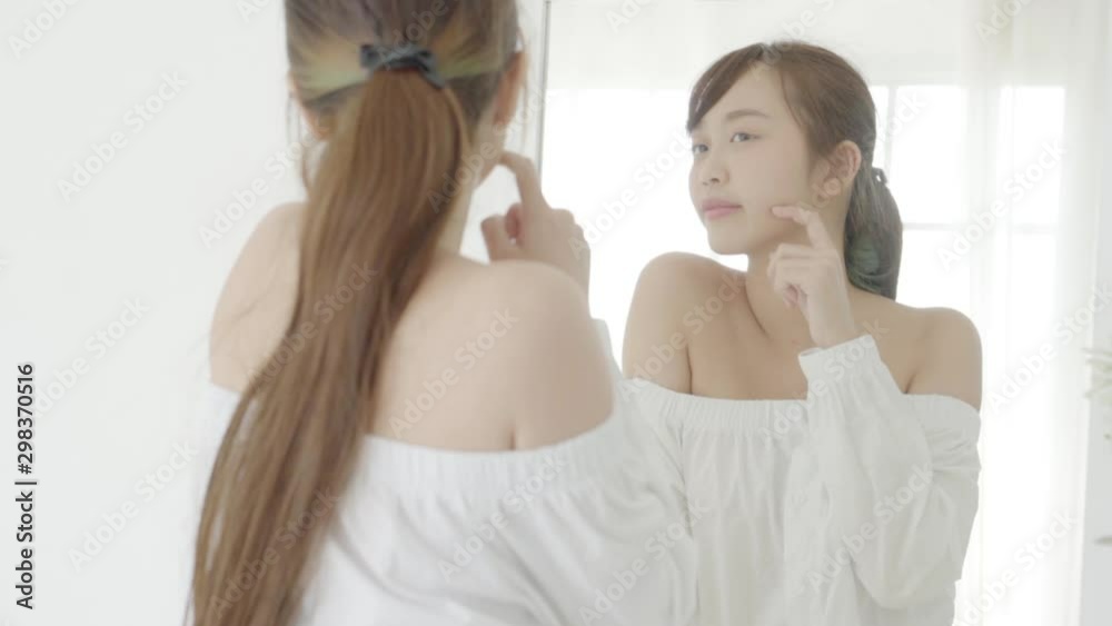 Beauty portrait young asian woman smiling look at mirror of checking skin care caucasian with wellness in the bedroom, beautiful girl happy face for health, lifestyle and wellbeing concept. Beauty portrait young asian woman smiling look at mirror of checking skin care caucasian with wellness in the bedroom, beautiful girl happy face for health, lifestyle and wellbeing concept.