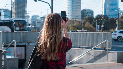 Tourism concept. Young woman with beautiful hair taking photo on smartphone while walking by the city.