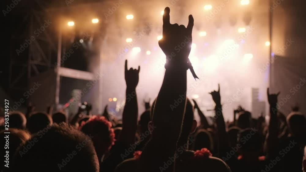 Silhouettes of fans at a music show, concert. Festival of youth rock music. Laser stage show. A crowd of fans raised their hands, applause. Rock symbol made of fingers. Rock concert. Lifestyle