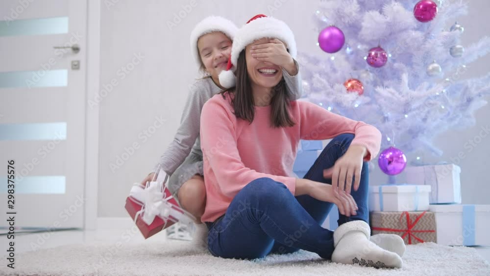 Small kid comes up on her mother from behind, closes mother's eyes with hand and gives her a present. They are hugging and touching with noses. Small kid comes up on her mother from behind, closes mother's eyes with hand and gives her a present. They are hugging and touching with noses.