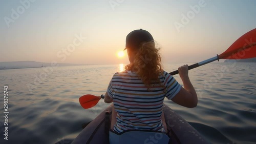 Happy young woman with her dog Jack Russell Terrier paddling on an inflatable kayak water lake a large mountain lake against orange sunrise slow motion slide. Family Sports Weekend. Lens flare. Gopro