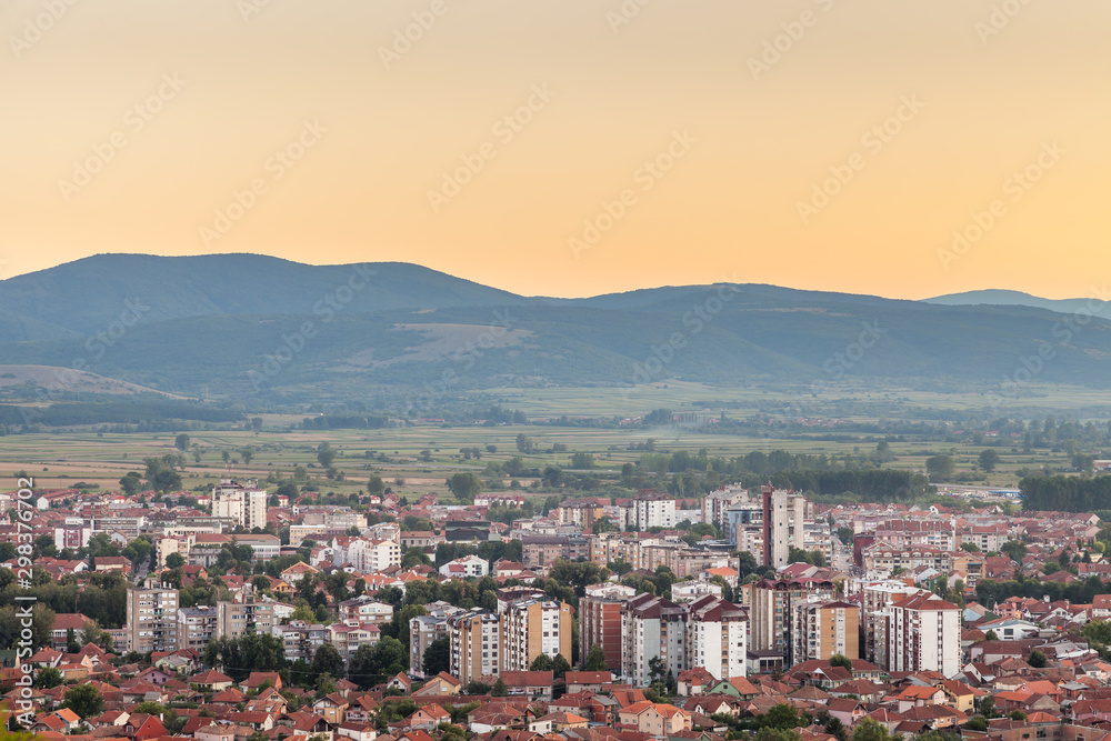 Beautiful golden hour sky above Pirot cityscape with buildings lighten by setting sun, city lights and car trails
