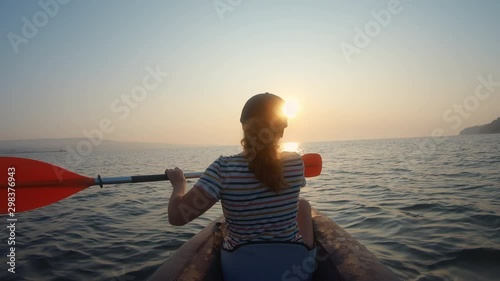 Happy young woman with her dog Jack Russell Terrier paddling on an inflatable kayak water lake a large mountain lake against orange sunrise slow motion slide. Family Sports Weekend. Lens flare. Gopro