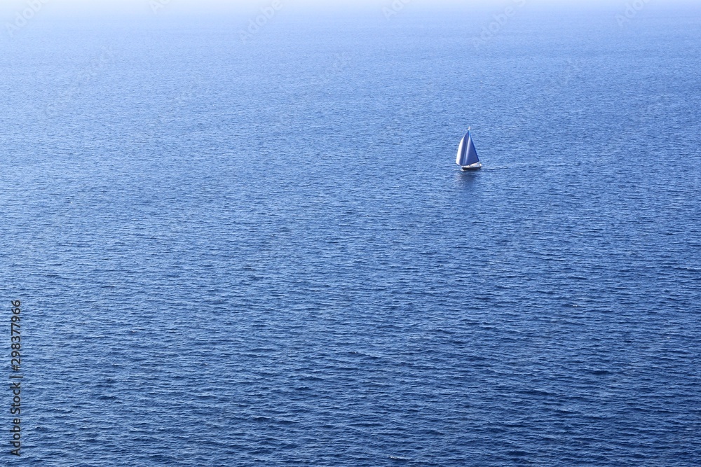 Alone sailing boat isolated in the middle of the ocean surrounded by deep blue sea water, travel at the unknown 