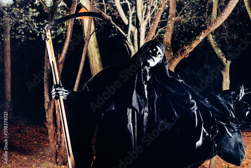 Grim Reaper standing in the fog at night with his scythe. photo