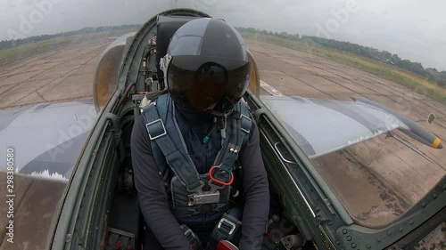 The pilot close helmet and looks around. Gray blue fighter combat aircraft accelerate on the runway at old airfield on a cloudy day. Inside view of cockpit. The plane moves on concrete slabs.