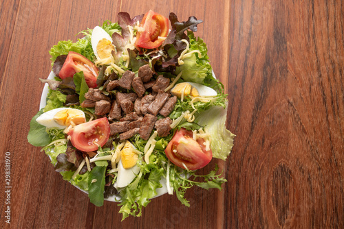 Fresh green salad with arugula,romaine, tomato, eggs, steak mignon and lettuce in a bowl on a wooden background