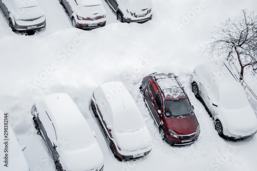 Parked cars and the road are covered with smooth layer of snow but one red car from them are cleared from snow and ice. Top view, aerial photography. Winter, daytime