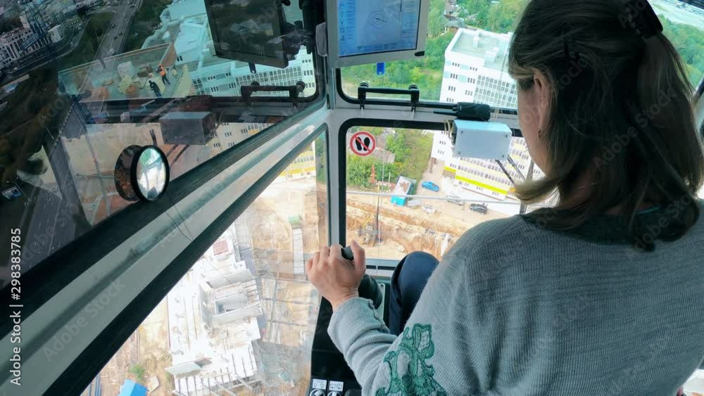 A woman is sitting in the cabin and operating a building crane