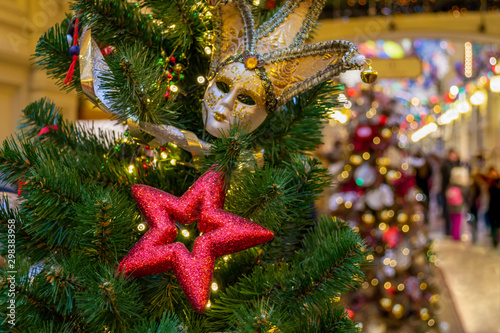 Christmas decorations. Red stars, masquerade mask, silver ribbons decorate the Xmas tree. Festive interior in the background. Indoor. Bokeh. Close-up