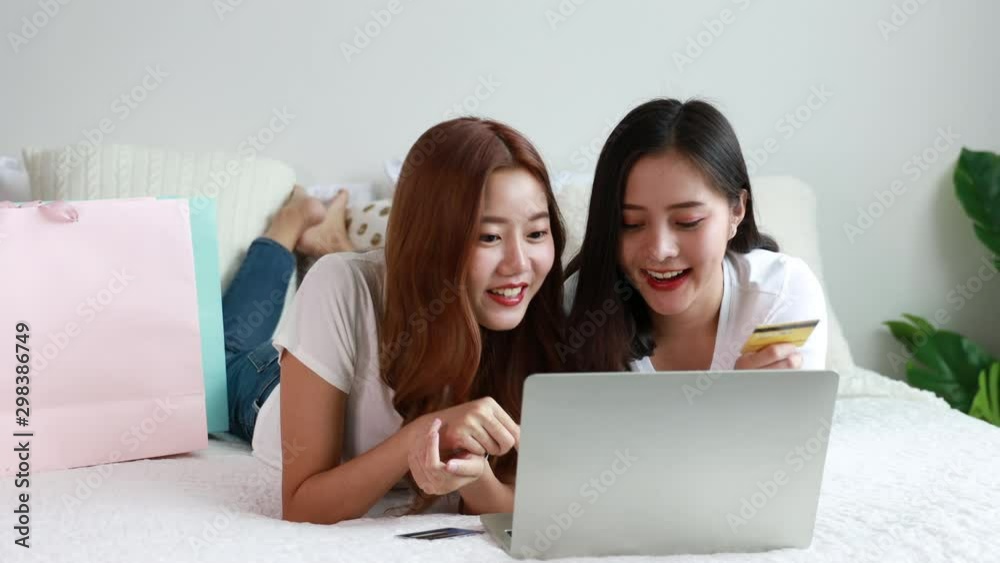 Happy Asian woman shopping online with laptop and credit card on bed in bedroom at home Happy Asian woman shopping online with laptop and credit card on bed in bedroom at home