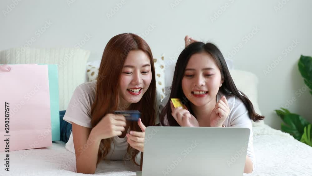 Happy Asian woman shopping online with laptop and credit card on bed in bedroom at home Happy Asian woman shopping online with laptop and credit card on bed in bedroom at home