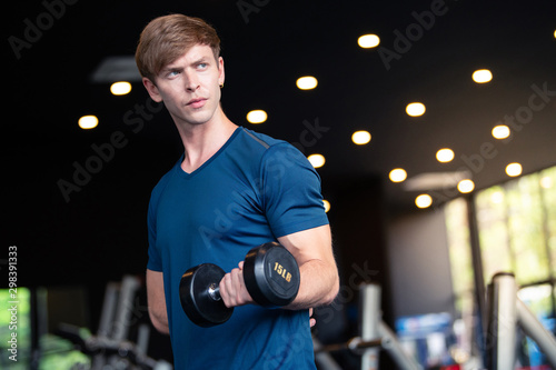 Portrait of young Caucasian man model hand holding dumbbell for biceps curl exercise in modern fitness gym