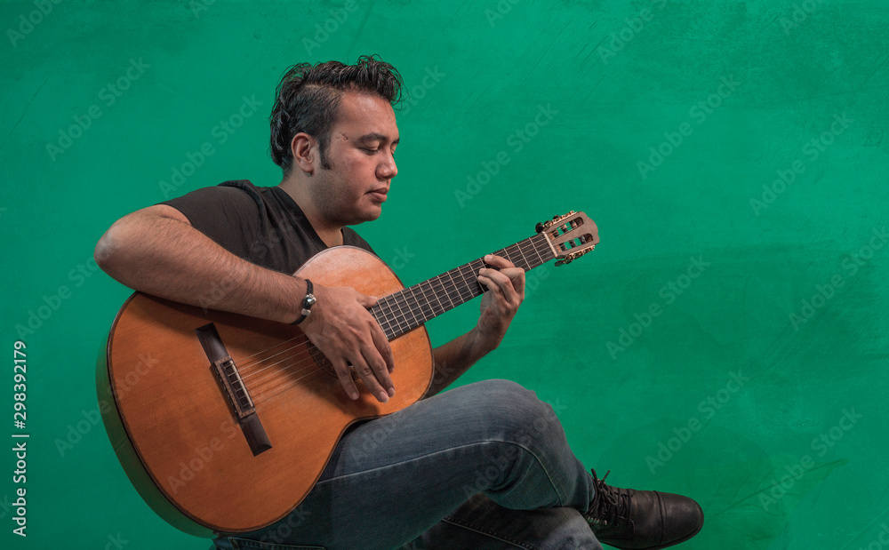 Obraz premium Young mexican with dark skin, latin playing guitar on green background