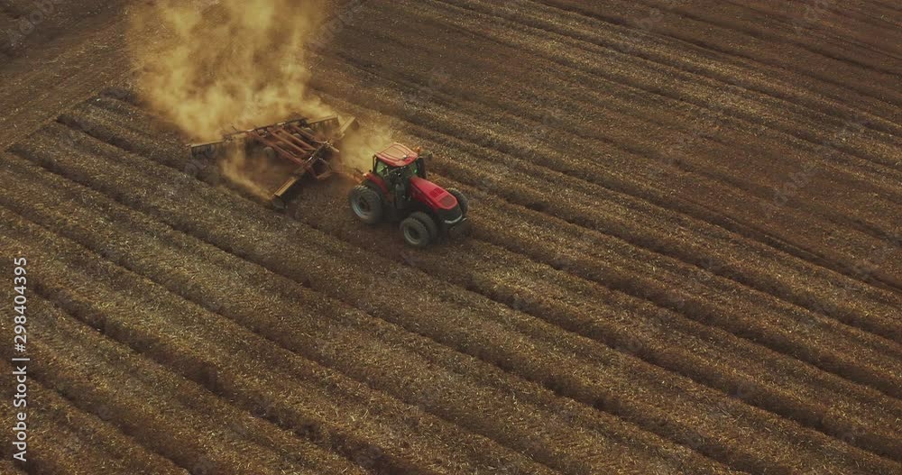 Aerial view of a farmer driving a red tractor through dusty fields at sunset with golden dirt rising into the air, farming at sunset, climate change barren dusty fields