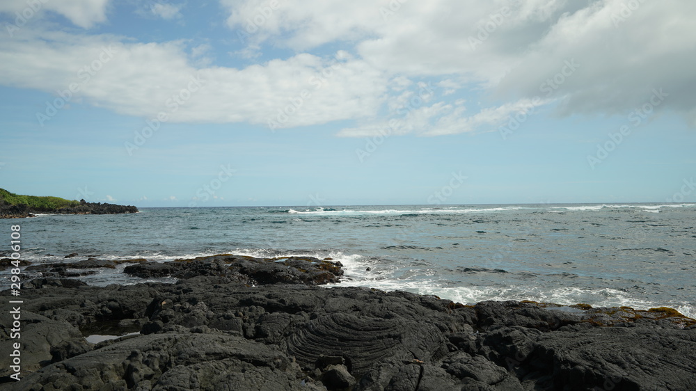 black molten lava rocky formation shore, ocean water waves, cloudy blue sky
