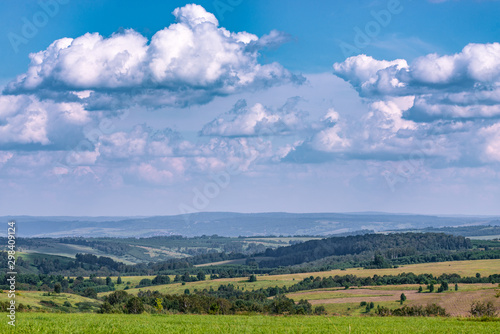 View of agricultural field with white fluffy clouds in blue sky at sunny summer day