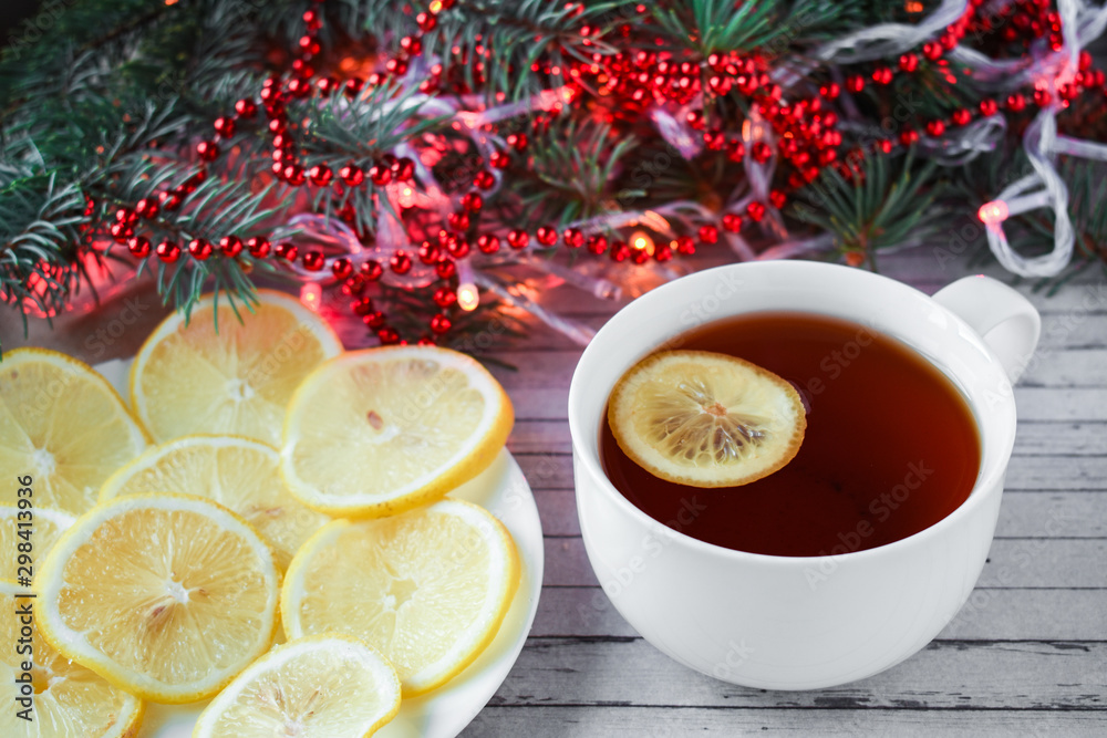 White cup of tea with lemon. New Year's decor, pine branches. A wooden background with Christmas decorations. A cup of hot tea with lemon. White cup of tea with lemon. New Year's decor, pine branches. A wooden background with Christmas decorations. A cup of hot tea with lemon.