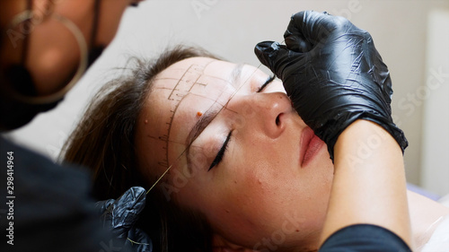 The process of shaping eyebrows by a beauty master with a thread for a young lady in the studio before the microblading. Close up view of a face while the procedure of marking lines. photo