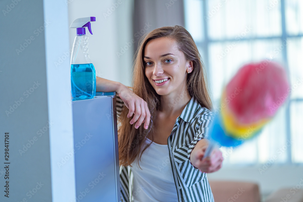 Portrait of young happy joyful cleaning woman with a dust brush during cleaning home. Household chores and housekeeping, housework Portrait of young happy joyful cleaning woman with a dust brush during cleaning home. Household chores and housekeeping, housework