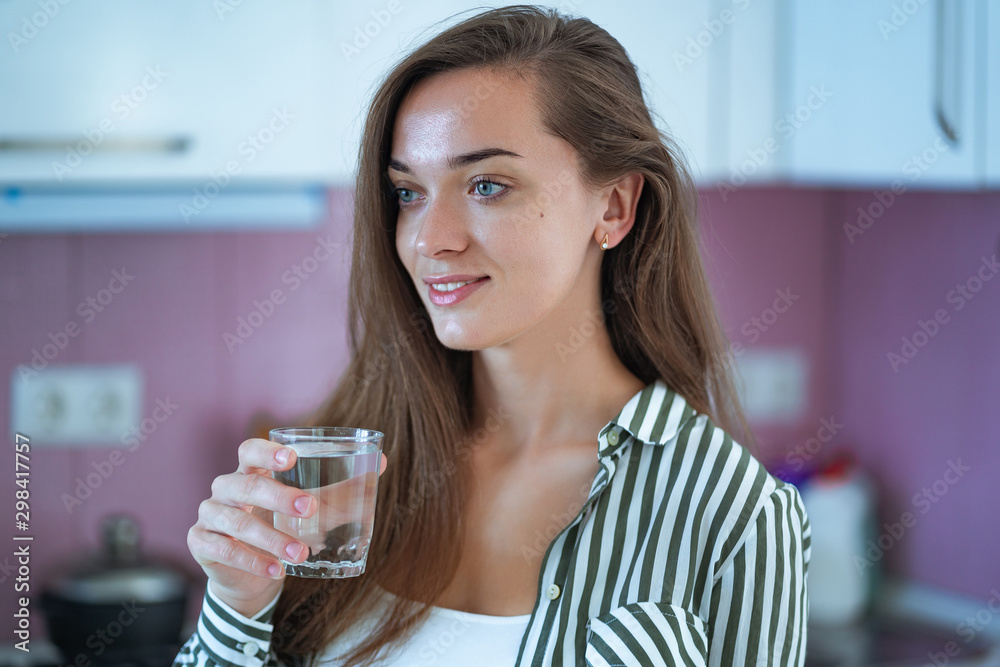 Happy attractive young woman holding a glass of clear purified water in the kitchen at home. Healthy lifestyle Happy attractive young woman holding a glass of clear purified water in the kitchen at home. Healthy lifestyle