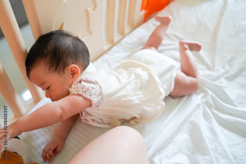 An Asian infant seven months old baby girl try to creep on her bed sheet in
