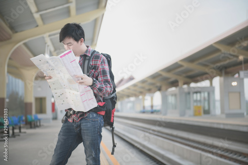 Young asian traveling backpacker wearing a red plaid shirt, sunglasses and looking a paper map at train station. Vintage tone. Travel concept.