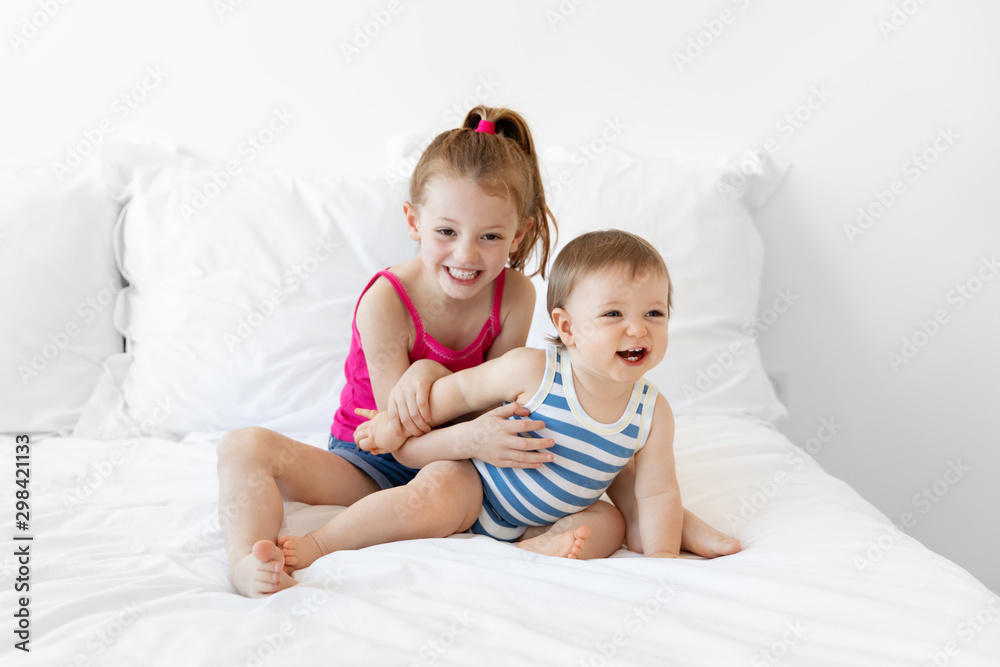 Baby boy and big sister having fun on white bed Baby boy and big sister having fun on white bed