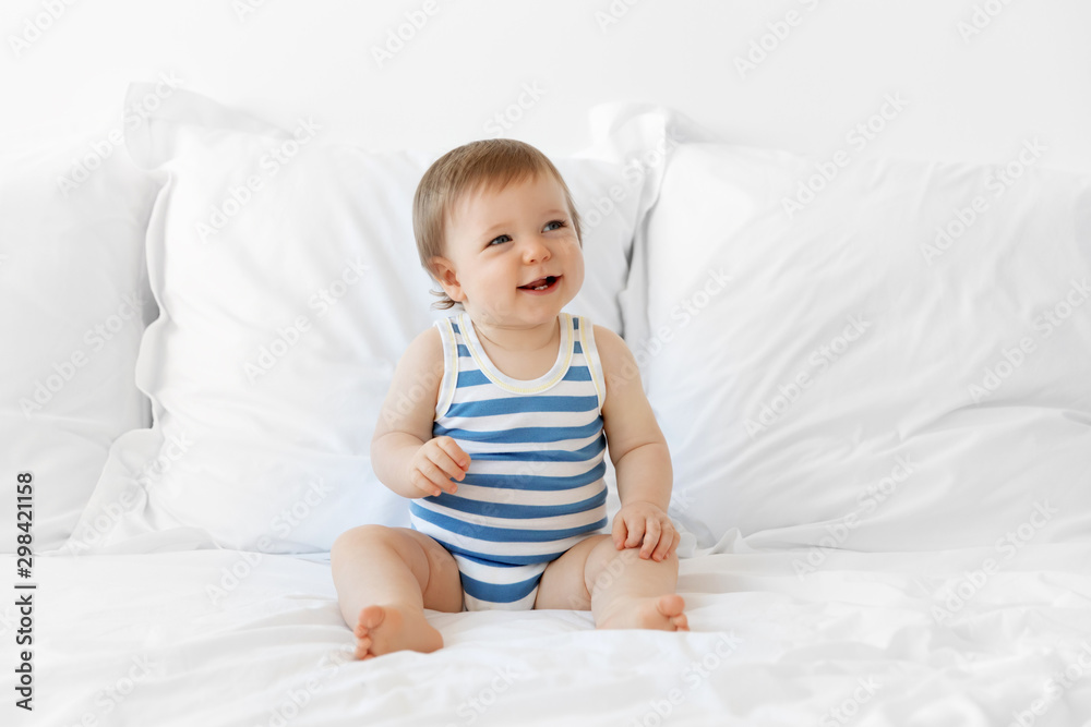 Smiling baby boy sitting on bed wearing striped onesie