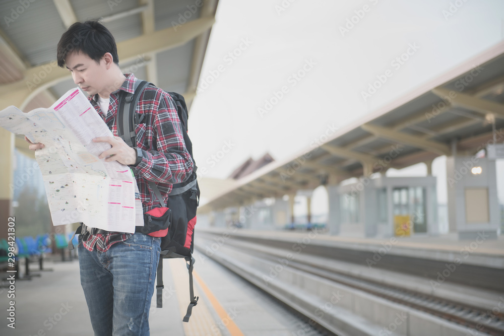 Young asian traveling backpacker wearing a red plaid shirt, sunglasses and looking a paper map at train station. Vintage tone. Travel concept.