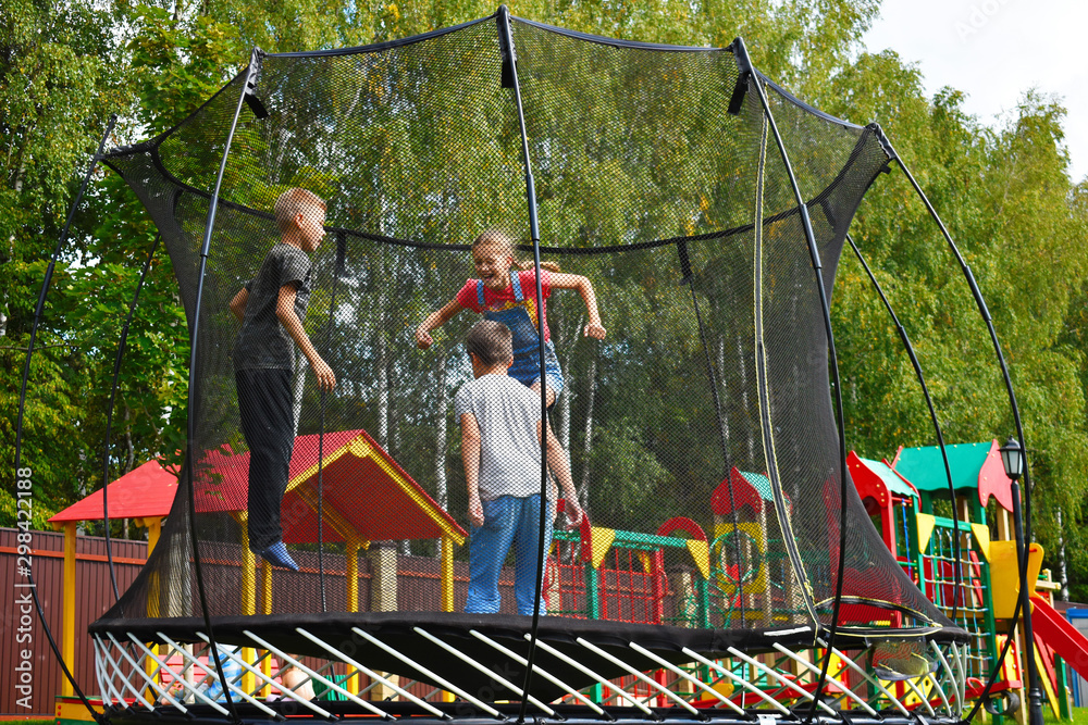 Children jump on a trampoline on summer. Cheerful happy childhood on the playground.