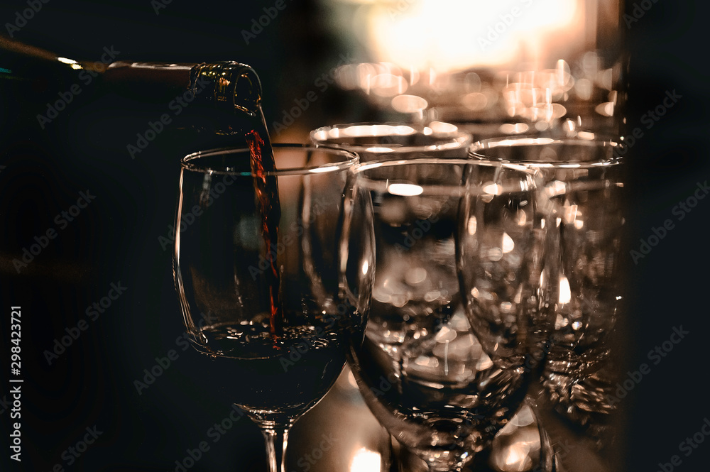 The bartender is pouring red wine in glasses and many empty glasses on the bar counter. Blurred background