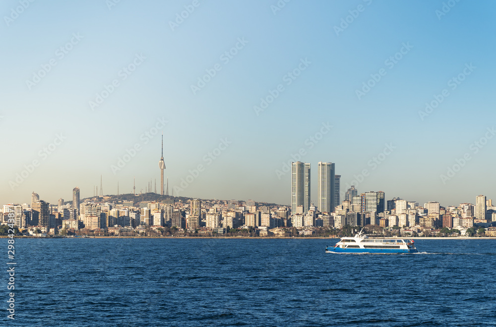 A pleasure ship floats against the backdrop of skyscrapers and residential buildings of the Asian side of Istanbul. One can see a high well-recognizable television tower.