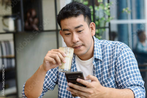 Smart Asian man using smartphone in cafe and drinking coffee, lifestyle concept.