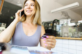 Blonde girl talking by smartphone and keeping debit card in hands.