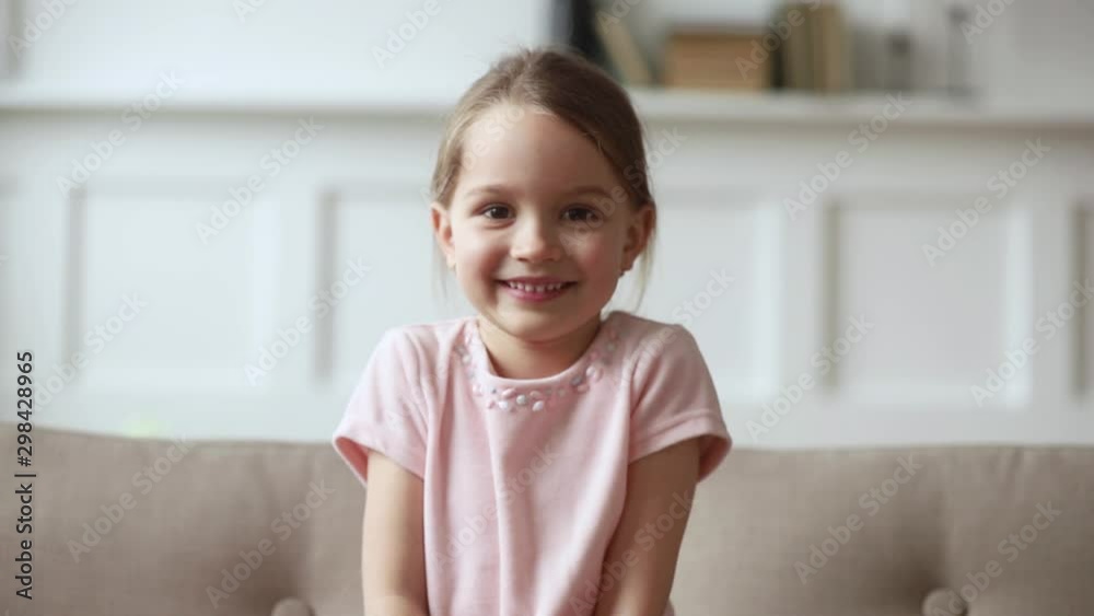 Little girl sitting on couch wave hand looking at camera Little girl sitting on couch wave hand looking at camera