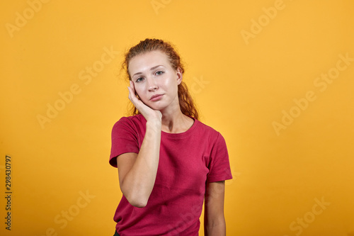 Young European woman keeping her right hand on cheek pretending a toothache. Pretty girl in pinky clothing with long wavy dark hair is over isolated yellow background.