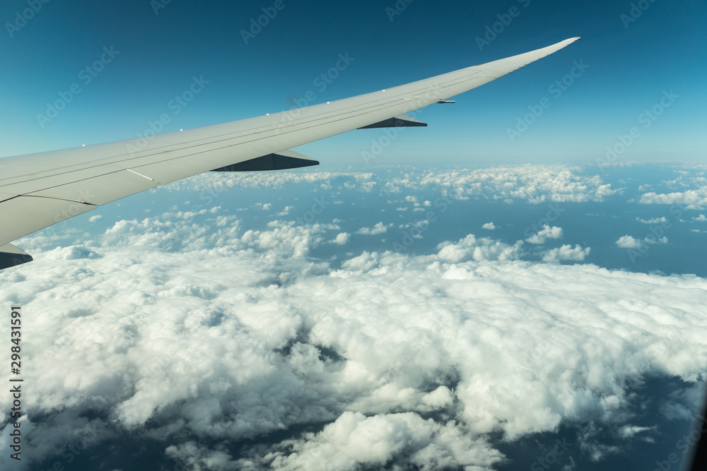 Fototapeta premium Plane’s wing above the clouds view from a plane's window with the blue sky.