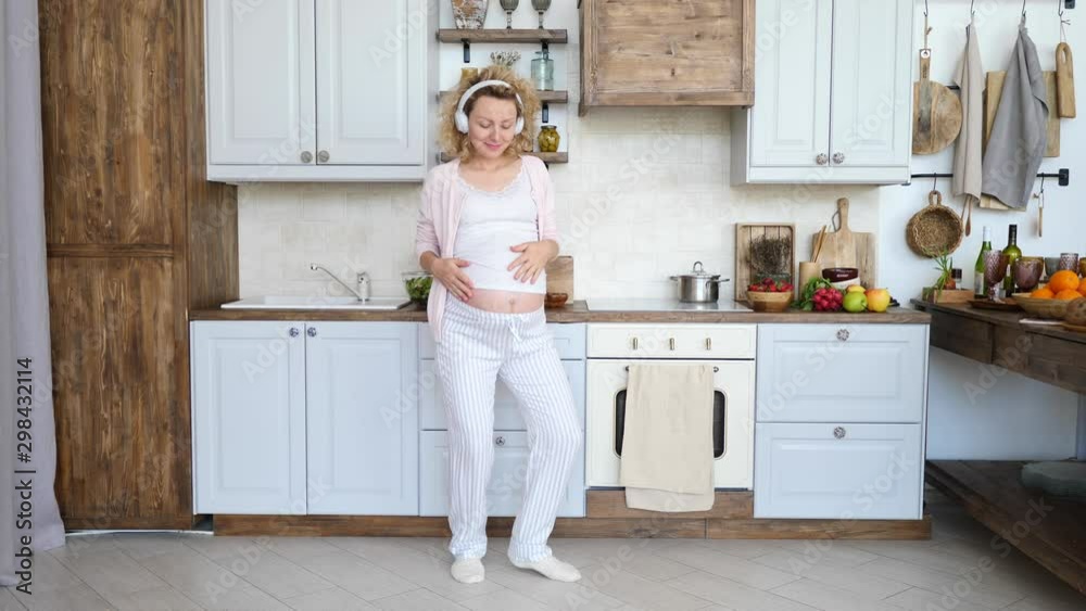Happy Pregnant Woman Wearing Headphones Dancing In Kitchen. Happy Pregnant Woman Wearing Headphones Dancing In Kitchen.